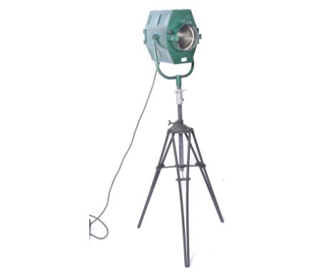 A mid century vintage film - theatre spot light being raised on a large vintage Photax tripod base. The green painted lamp wi