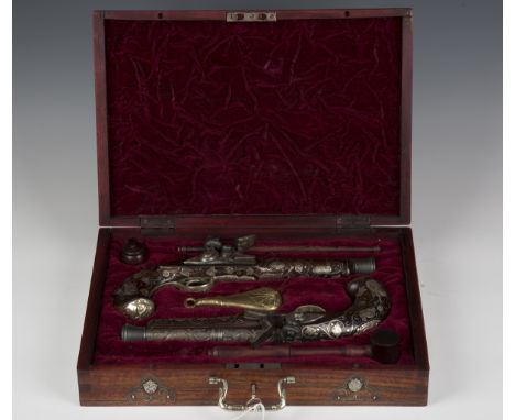 A pair of 20th century Indian flintlock pistols with profuse inlaid white metal foliate decoration and mask shaped butt caps,