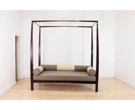 A stained wooden four-poster daybed, of recent manufacture, with cream and grey rectangular seat and bolster cushions, within