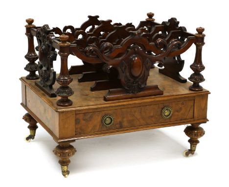 A Victorian walnut canterbury,with four scrolled sections and a base drawer, raised on turned supports and ceramic casters,66