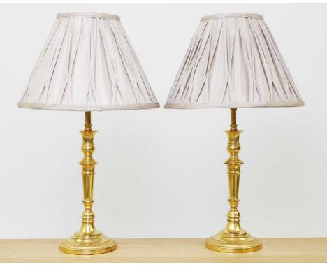 A pair gilt bronze candlestick lamps,mid-20th century, each with a taupe silk pleated shade,12cm diameter50cm high with shade