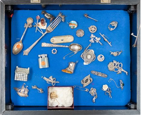 A display cabinet containing silver and white metal brooches, fork, spoons and costume jewellery etc