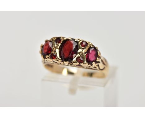 A 9CT GOLD THREE STONE GARNET RING, designed with a row of three graduated oval cut garnets, interspaced with circular cut ga