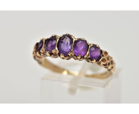 A 9CT GOLD FIVE STONE AMETYHST RING, designed with a row of five graduated oval cut amethyst, scroll detailed shoulders, hall