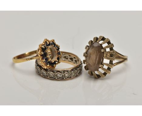 A 9CT GOLD DRESS RING AND TWO YELLOW METAL RINGS, the first of an oval shape set with an oval cut smoky quartz, within a rais