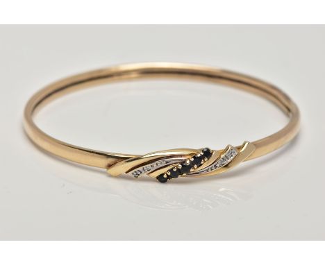 A 9CT GOLD SAPPHIRE AND DIAMOND HINGED BANGLE, the centre designed with a curved cross over section, set with a row of circul