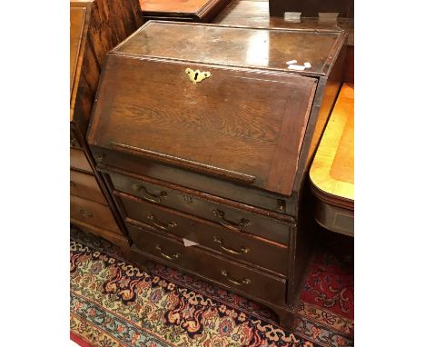 An 18th Century oak bureau of small proportions the plain top over a sloping fall enclosing a fitted interior with pigeon hol