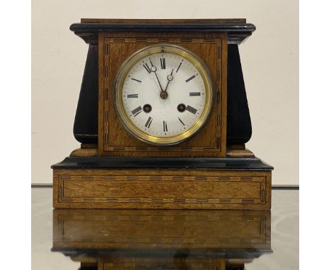 A late 19th / early 20th century mantel clock, the oak and ebonised case with chequered inlay enclosing a white enamel dial w