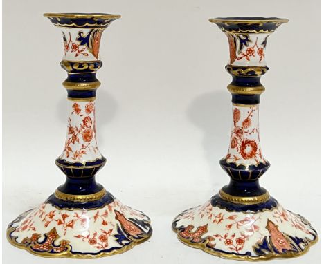 A pair of Royal Crown Derby Imari palette candlestick holders decorated with red transfer printed floral designs and Rococo s