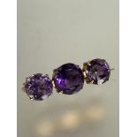 A Edwardian yellow metal amethyst three stone graduated brooch in four claw setting, the center