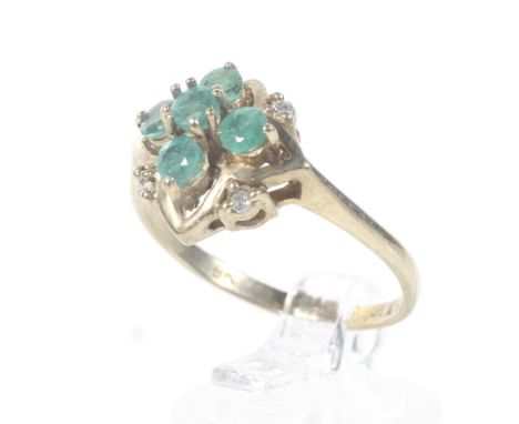 A modern 9ct gold, emerald and diamond cluster ring. The five round mixed-cut emeralds with tiny eight-cut diamond points in 