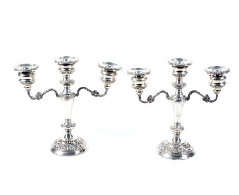 A pair of silver two branch/three light candelabra. Each with beaded nozzles, floral embossed capitals, knoped stems and roun