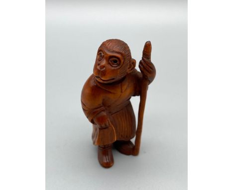 A Japanese hand carved netsuke of a Monkey God figure, Designed holding a staff and wearing a robe. Set with black bead eyes.