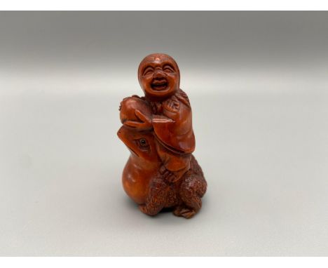 A Japanese hand carved netsuke of an elderly chap riding on top of a toad. Toad is detailed with black bead eyes and signed b