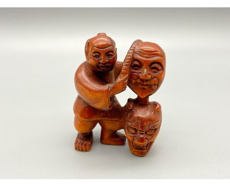A Japanese hand carved netsuke of a gentleman selling oni masks. Signed by the artist. [4.5cm] 