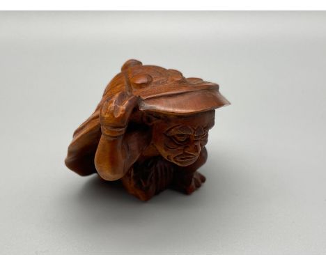 A Hand carved Japanese netsuke of an Oni Monster carrying a large samurai style hat. Signed by the artist. [3cm height] 