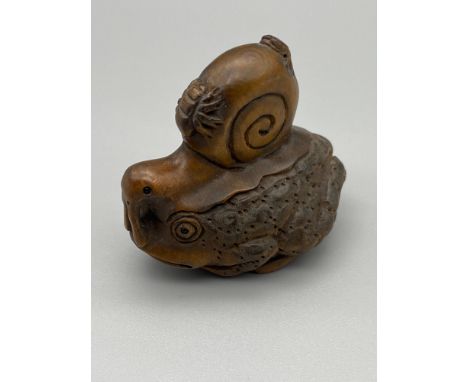 A Hand carved Japanese netsuke of a large toad with a snail sat upon the toads back and two bugs on top of the shell of the s