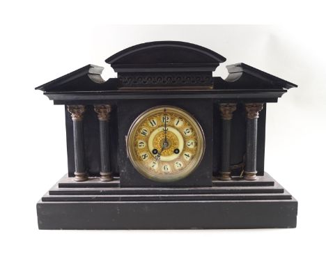 A black stone Temple style mantel clock with four brass topped corinthian columns to the front and a central brass dial with 