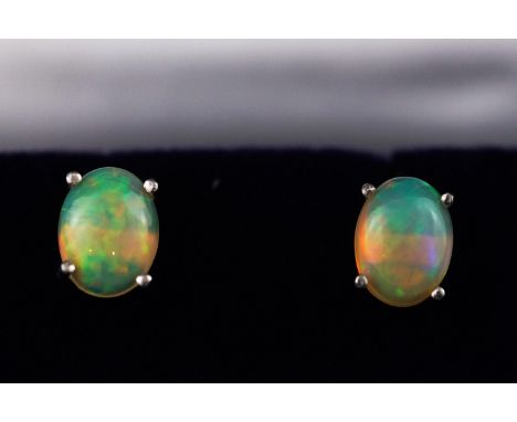 A modern white metal pair of single stone stud earrings each set with an oval cabochon Ethiopian opal. Post and scroll fittin