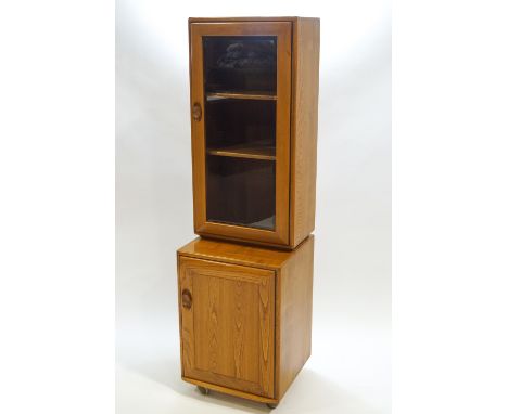 An Ercol elm wood standing cabinet of rounded rectangular form, the dove tailed glazed top with carved wood catch to the door