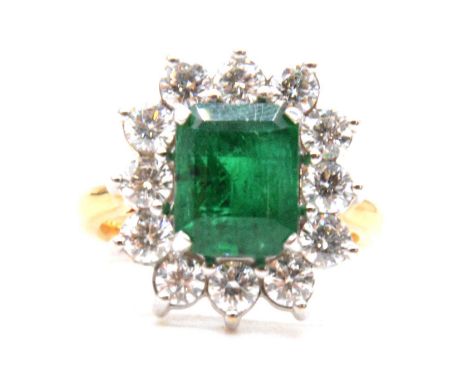 An emerald and diamond cluster ring, the emerald cut emerald, 10.2x8.3mm, surrounded by twelve 3.5mm diameter brilliant cut d