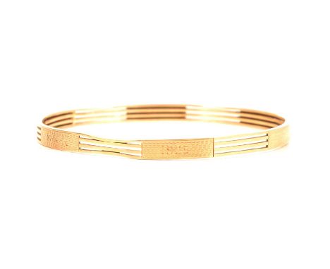 A yellow metal upper arm bangle, 5.6mm wide, four polished bars wide spaced by six engine turned plates, two engraved "B.M.K.