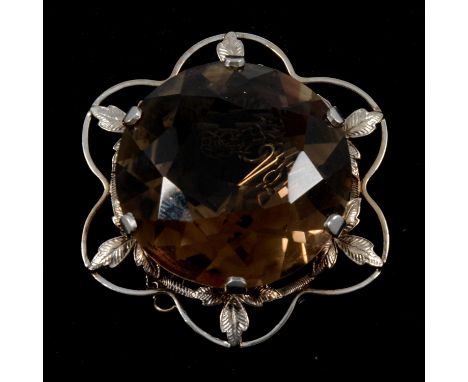 A smoky quartz brooch, the 29mm diameter circular brilliant mixed cut stone claw set in a pierced white metal mount with leaf