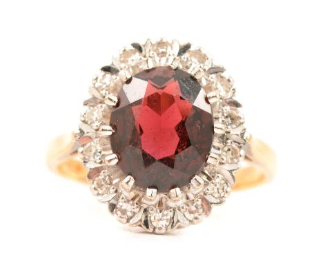 A garnet and diamond cluster ring, the oval mixed cut garnet 10x8mm, claw set and surrrounded by fourteen illusion set eight 