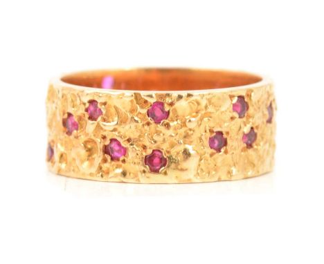 An 18 carat yellow gold band set with rubies, 7.5mm wide molten finish, the twenty rubies inset into the band, ring size K ce