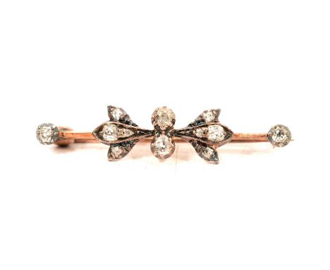 A small diamond brooch in fitted box, the 35mm long rose metal bar having a bow motif to centre and terminations set with twe