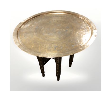 A Middle Eastern bobbin turned folding occasional table with brass top depicting Egyptian scenes, diameter 64 cm.