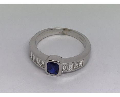 An 18ct white gold sapphire and channel-set diamond ring. Central emerald-cut sapphire 0.41ct approx. Baguette-cut diamonds s