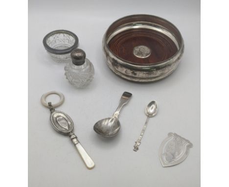 A selection of silver items to include a wine coaster, a silver and mother of pearl baby rattle, a tea caddy spoon, scent bot