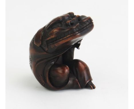 A Japanese carved hardwood netsuke depicting a man putting on a Dragons head costume, unsigned, 5cm long, Meiji period. 