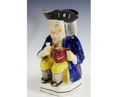 A 19th century Toby jug, seated holding a jug of beer, wearing a tricorn hat, cobalt blue jacket, canted square base, c.1830