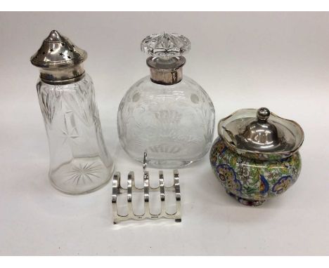 Silver toast rack, silver topped glass sugar sifter, silver collared etched glass decanter and silver topped ceramic preserve