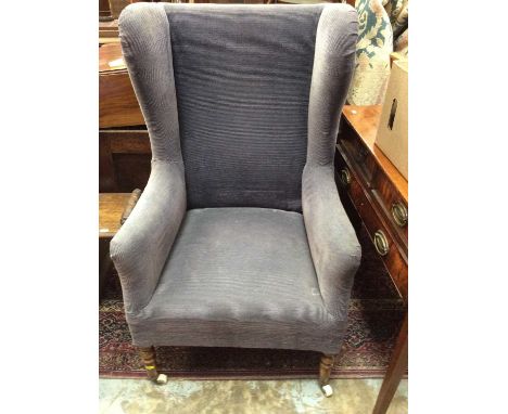 Antique wing back armchair upholstered in blue material on turned mahogany legs with ceramic castors