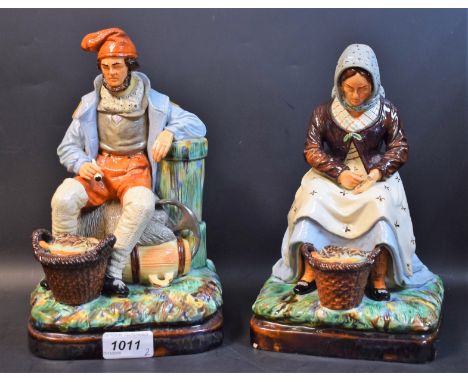A pair of 19th century Majolica figures, of a fisherman and fisherwoman, both seated with baskets of fish, in coloured enamel