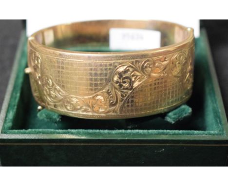 A 9ct gold hinged bangle, engraved with a wavy band of foliate scrolls on a hatched ground, Birmingham 1977, 38.5g, cased