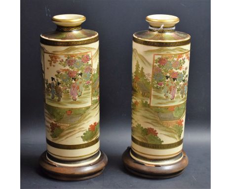 A pair of Japanese Satsuma cylindrical vases, decorated with mountains, figures and pagodas, 22cm high, wooden bases