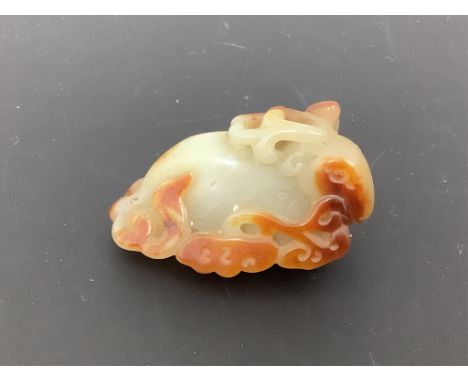 A Chinese pale celadon and russet skin jade figure of a stag, 19th century, the recumbent stag biting a sprig of lingzhi fung