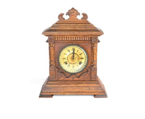 An oak cased Ansonia American mantel clock, the architectural case with scroll cresting, the pressed brass dial having black 