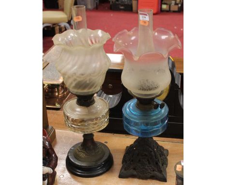 An early 20th century oil lamp, having a pink tinted etched glass shade above a blue glass font, on a pierced cast iron base,