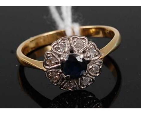 An 18ct gold, sapphire and diamond cluster ring, the four-claw set round cut sapphire in a surround of eight small round cut 