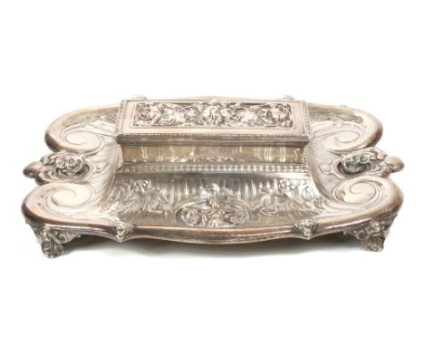 Victorian silver inkstand of scrolling form, inset with two panels of a child playing with a lion and two other separate face