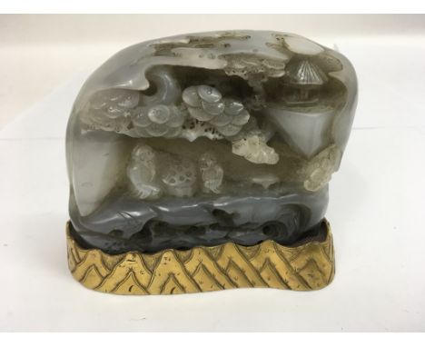 A grey jade carving depicting figures sheltering on a rocky ledge, mounted on gilt base.Approx 13x11cm high