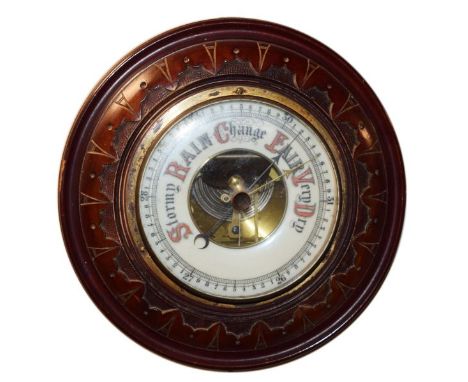 Early 20th Century circular carved walnut framed aneroid barometer, the off-white dial with a visible mechanism to the centre
