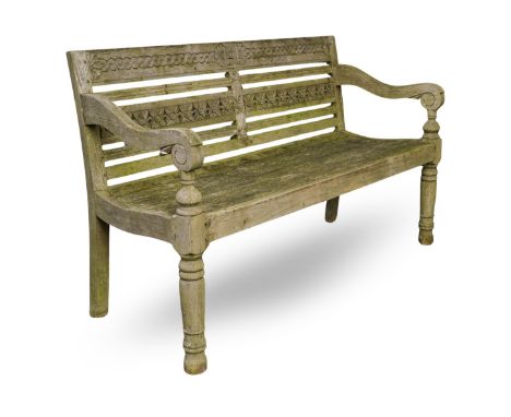 A well weathered garden bench, guilloche and foliate carved details to back, planked seat, scrolled arms, turned front legs, 
