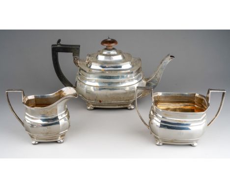 A George V silver three piece tea service of shaped rectangular form, on flattened bun feet, tea pot with circular finial and