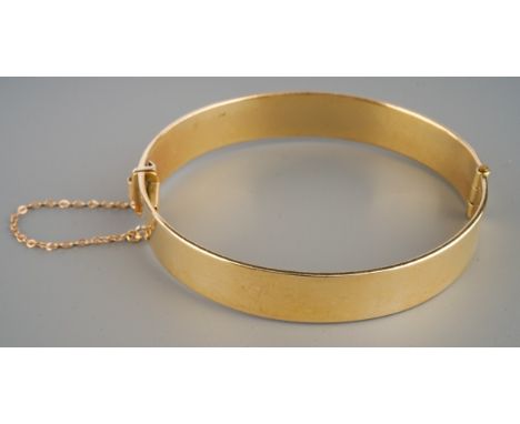 A 9ct gold plain bangle, hinged, fitted with safety chain, stamped 375 BREV, inner dimensions 57mm x 63mm, 35.6 grams